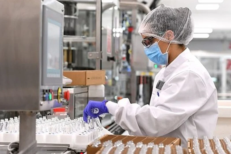 Une femme en charlotte qui manipule des flacons en industrie pharmaceutique